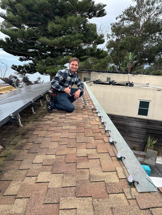 Dante G on a roof, clipping C9 bulbs along the gutter