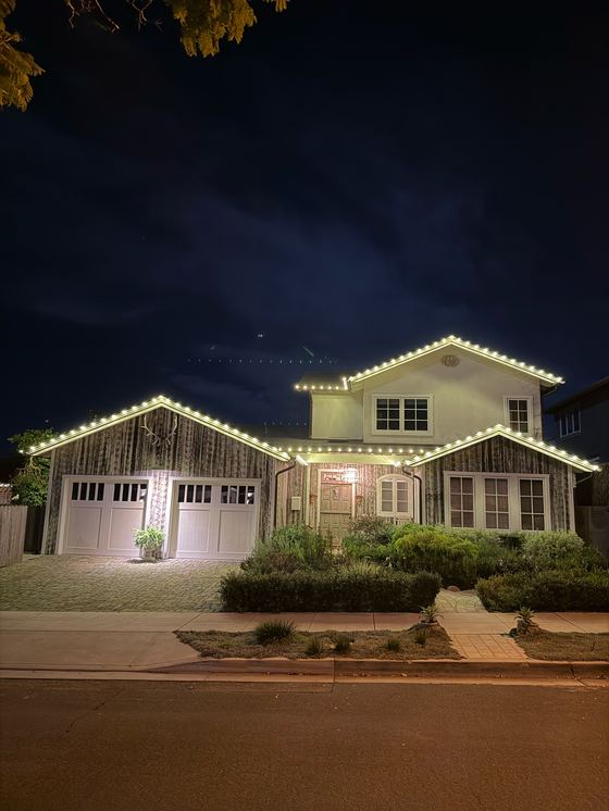 A two-story home at night with every roofline outlined in warm-white bulbs